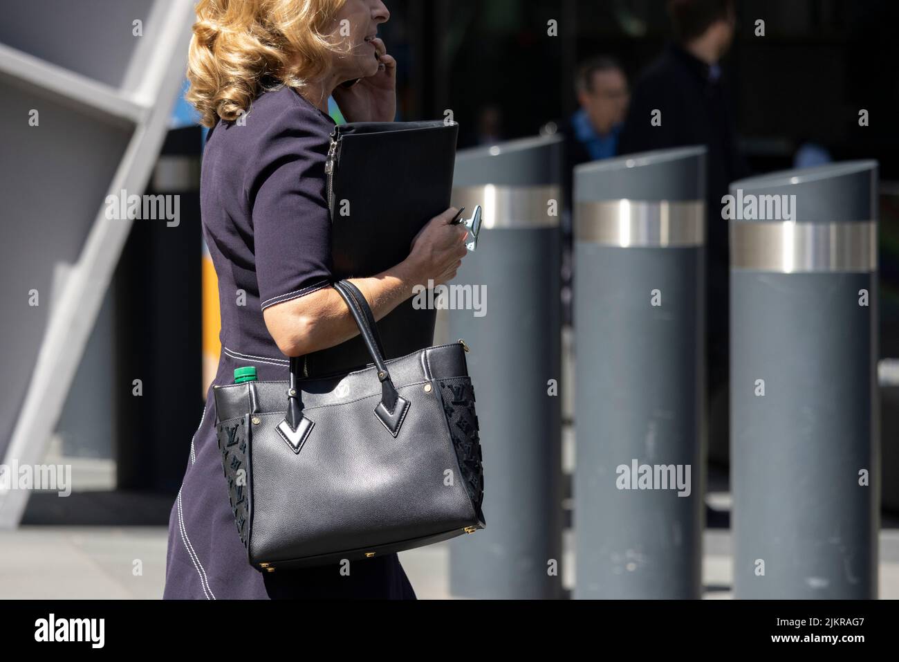 Geschäftsfrau, die während eines geschäftlichen Anrufs durch die City of London geht, London, Großbritannien Stockfoto