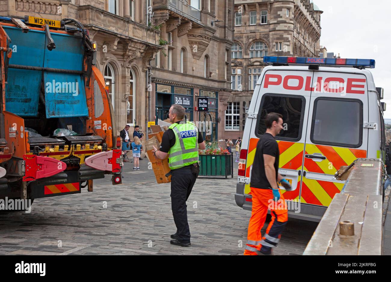 Stadtzentrum, Edinburgh, Schottland, Großbritannien. 3. August 2022. Wolkiger, dumpfer Morgen im Zentrum der Stadt für die Bewohner und Touristen war die Royal Mile mit Spaziergängen und ein paar Gruppen beschäftigt, die Flyer für EdFringe-Shows verteilten. Im Bild: Jenseits der Einsatzbereitschaft hilft ein sehr hilfsbereiter Poice Officer einem Müllsammler, Abfall auf den Wagen zu laden, während der Verkehr in der Royal Mile wieder anfängt zu steigen. Kredit: ArchWhite/alamy Live Nachrichten Stockfoto