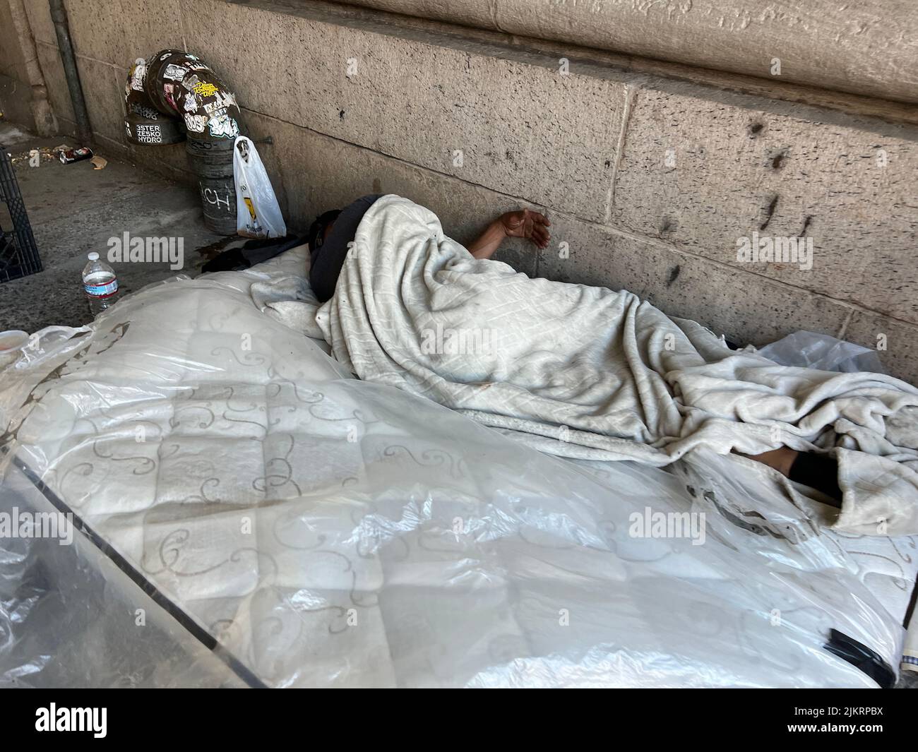 Der Mann schläft auf einer Matratze auf dem Bürgersteig mitten in Manhattan, New York City. Stockfoto