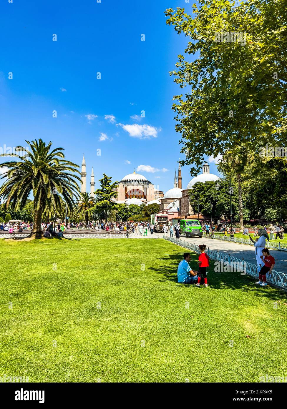 Istanbul - Türkei - 14. Juli 2022: Ruhende Touristenfamilie, die im Schatten einer schönen Palme vor der berühmten Hagia Sophia sitzt Stockfoto