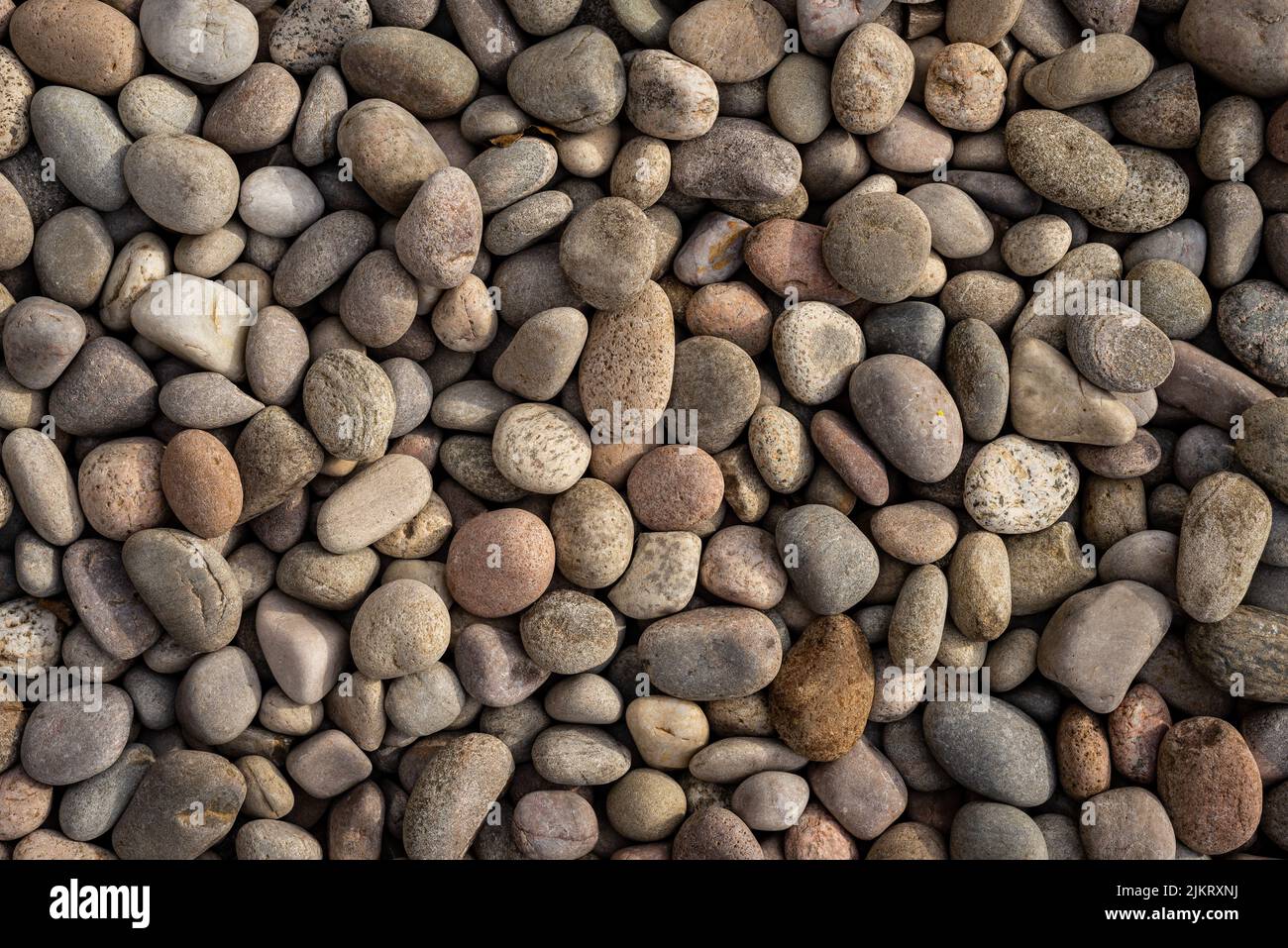 Abstrakter Hintergrund aus runden natürlichen unregelmäßigen rauen braunen und beigen Kieselsteinen. Stockfoto