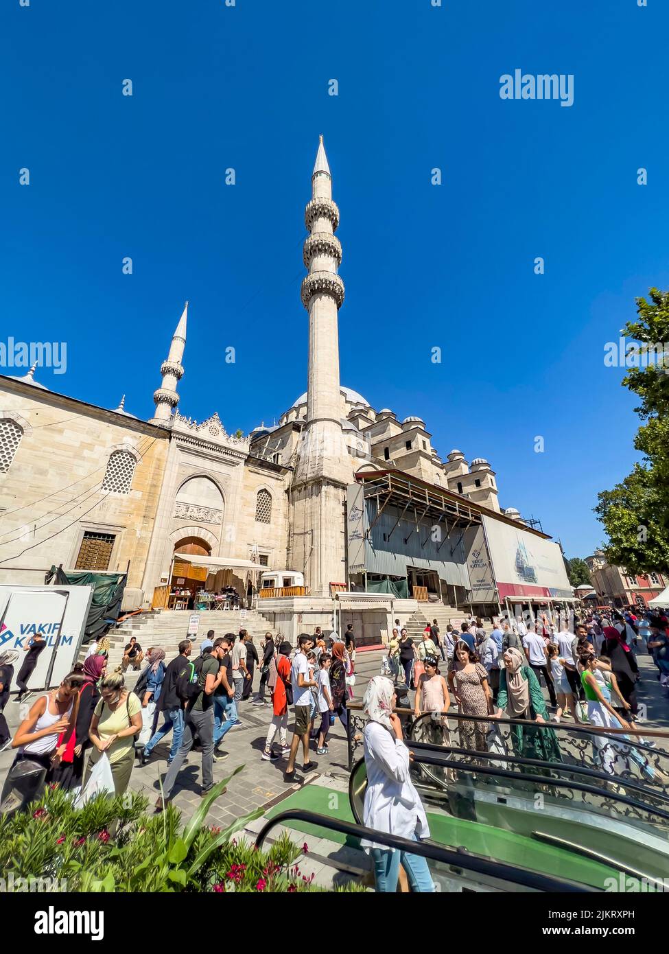 Istanbul, Türkei, 07.14.2022: Weitwinkelansicht des schönen Yeni Cami Minarett (Neue Moschee) Hinterhofs. Überfüllte Einheimische. Muslimische Männer und Hijab Schal Stockfoto