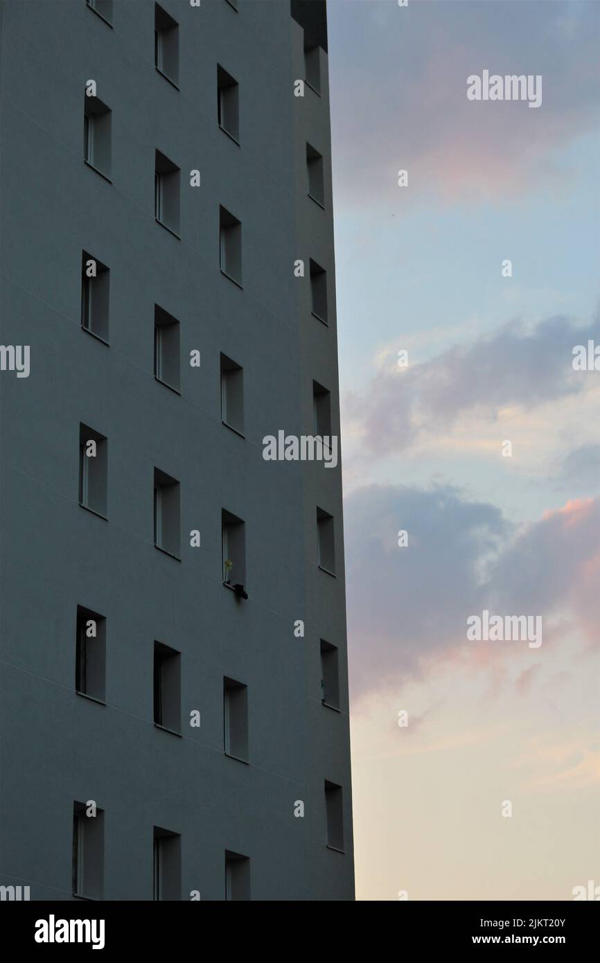 Schlichtes Betonwohnhaus mit symmetrischen rechteckigen Fenstern vor einem Sonnenuntergangshimmel mit bunten Wolken. Konzept für urbane Symmetrie, modern Stockfoto