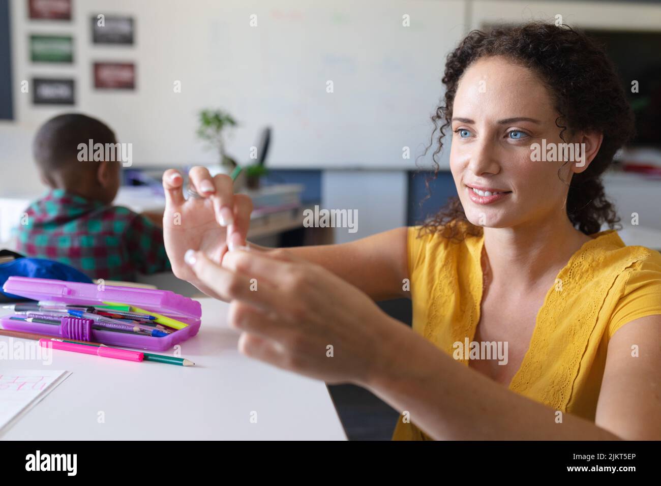 Lächelnde kaukasische junge Lehrerin, die im Klassenzimmer durch Gebärdensprache unterrichtet Stockfoto