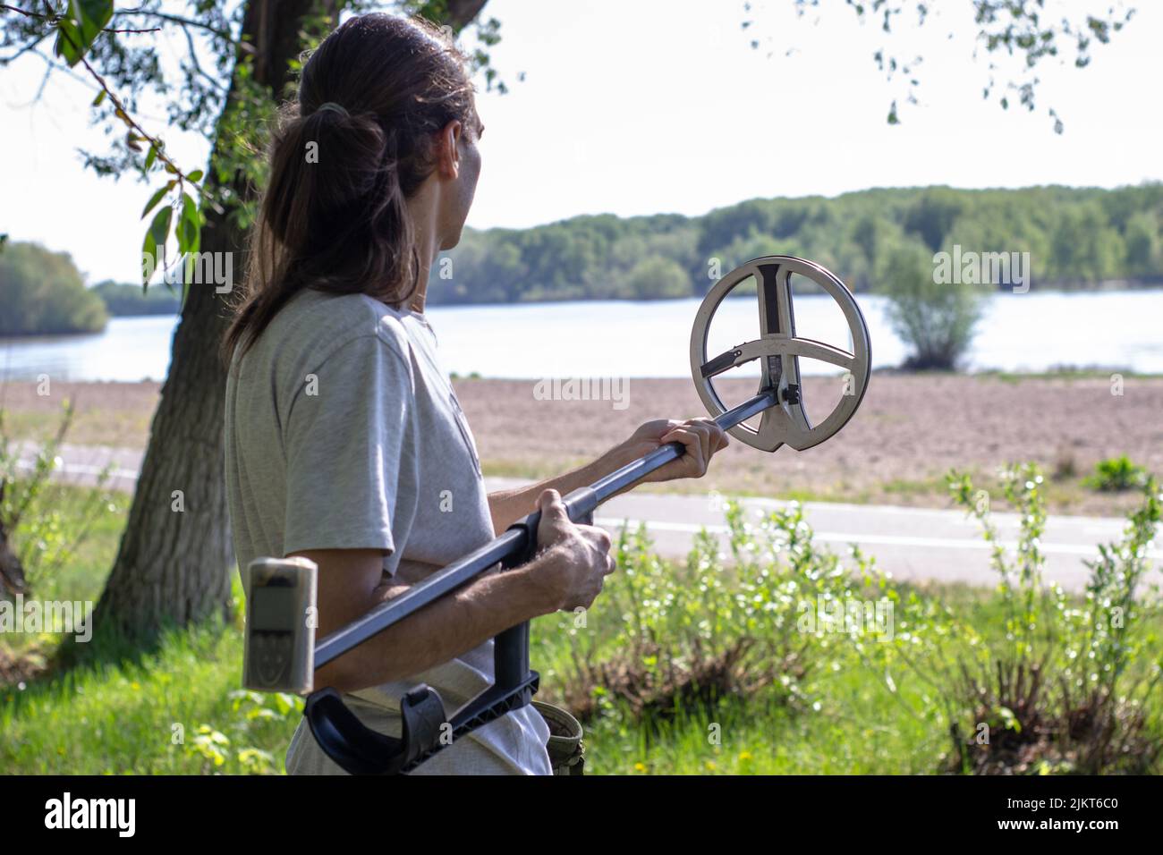 Junger Mann, der am Flussufer einen faltbaren drahtlosen Metalldetektor zusammenführt Stockfoto