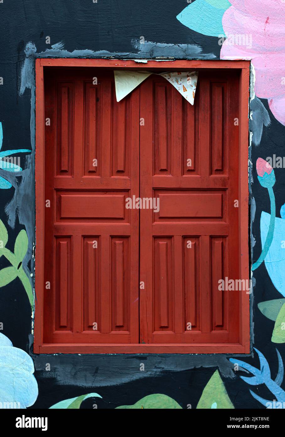 Nahaufnahme eines kleinen Fensters mit roten Fensterläden aus Holz auf einem bunt bemalten Gebäude Stockfoto