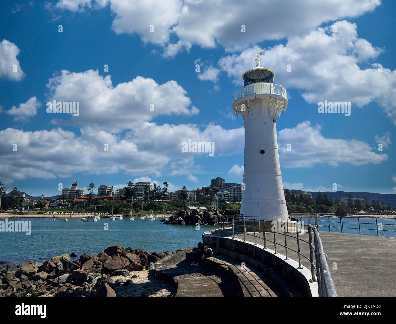Ein weißer Leuchtturm am Eingang zum Hafen von Wollongong und ein Yachthafen an der Küste vor blauem Himmel und flauschigen Wolken Stockfoto