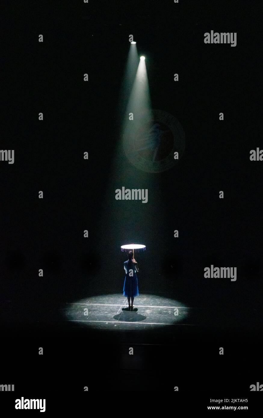 Eine vertikale Rückansicht einer Person auf der Bühne, die einen Schirm hält, der von Bühnenlaternen beleuchtet wird Stockfoto