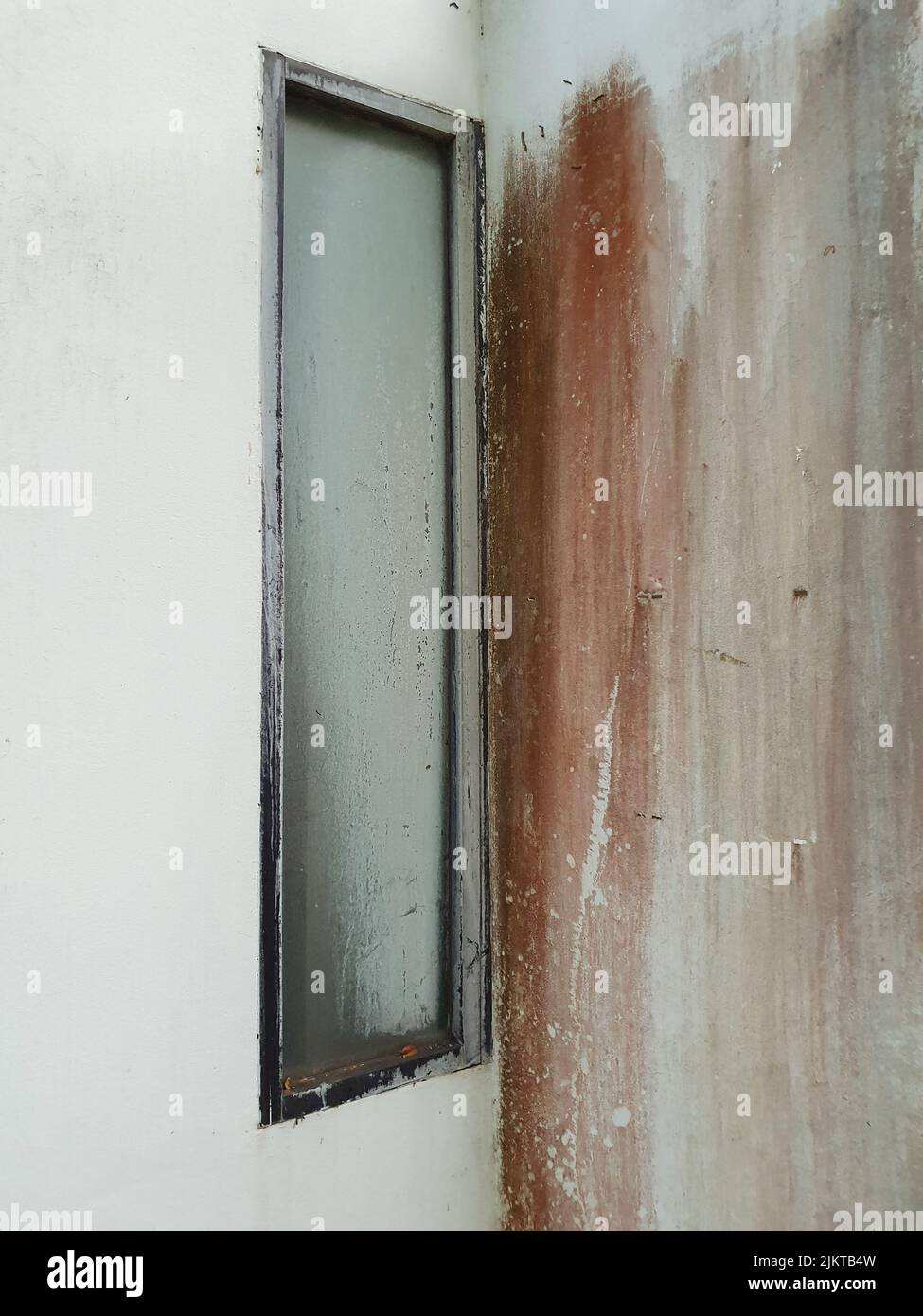 Ein altes, geschlossenes graues Fenster in einem Raum mit weißen Wänden und braunen Farben, die mit einem Pinsel gemalt wurden Stockfoto