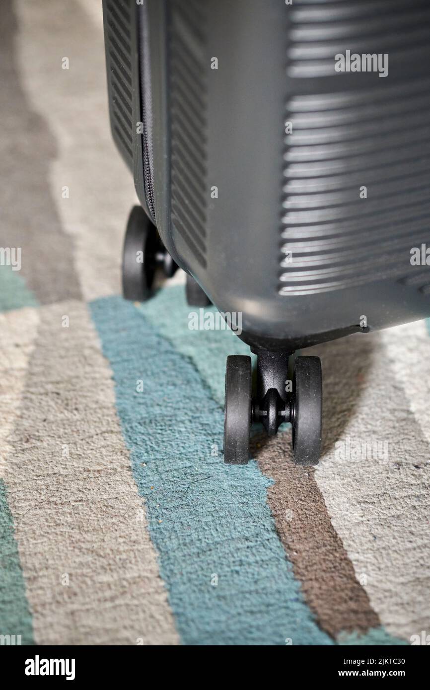 Eine vertikale Nahaufnahme eines schwarzen Reisekoffers rollt auf dem Teppich. Stockfoto