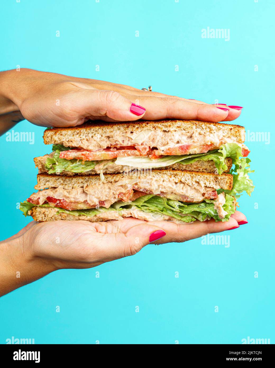 Eine vertikale Aufnahme eines Weibchens, das ein Thunfisch-Sandwich in der Hand hält Stockfoto
