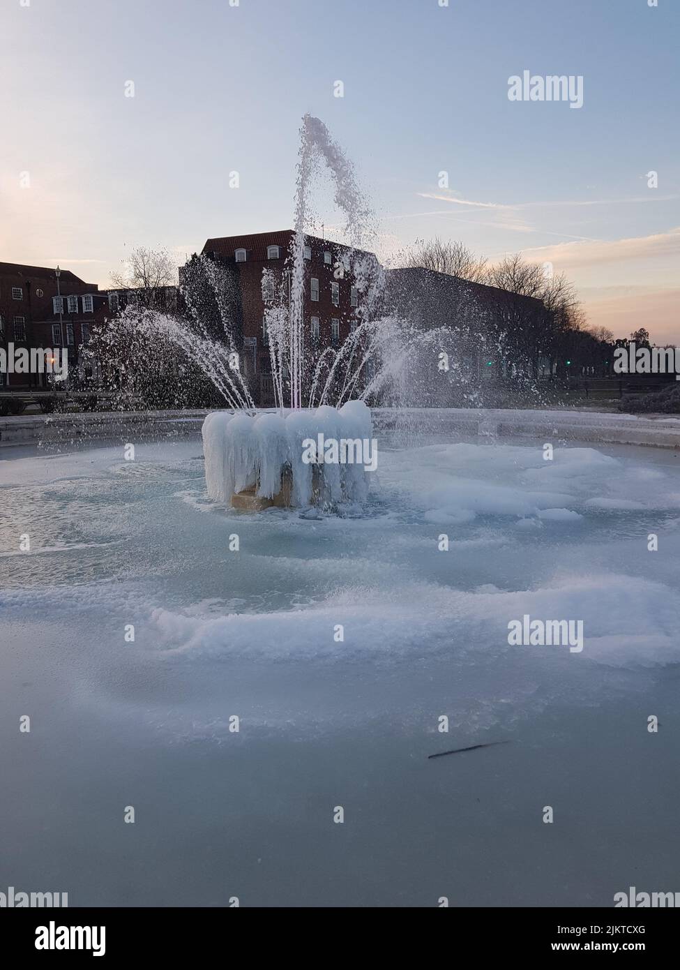 Ein gefrorener Brunnen, der mit Eis bedeckt ist, und Gebäude im Hintergrund Stockfoto