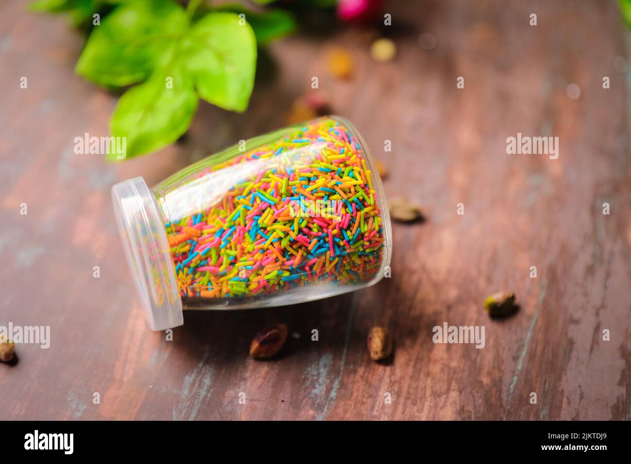Eine Nahaufnahme eines durchsichtigen Glases, gefüllt mit bunten Funkeln für Dekorationen auf einem Holztisch Stockfoto