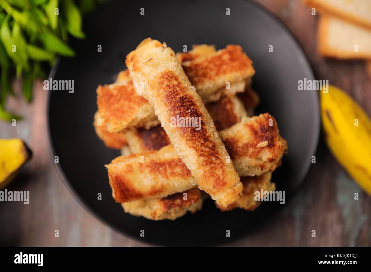 Eine Draufsicht auf frittierte gefüllte Brotstäbchen, die auf einem schwarzen Teller auf einem Holztisch gestapelt sind Stockfoto