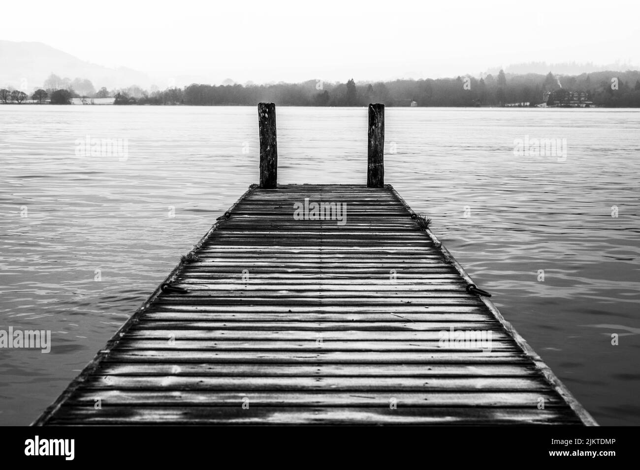 Die wunderschöne monochrome Aufnahme eines hölzernen Piers mit einer wunderschönen Seenlandschaft im Hintergrund Stockfoto