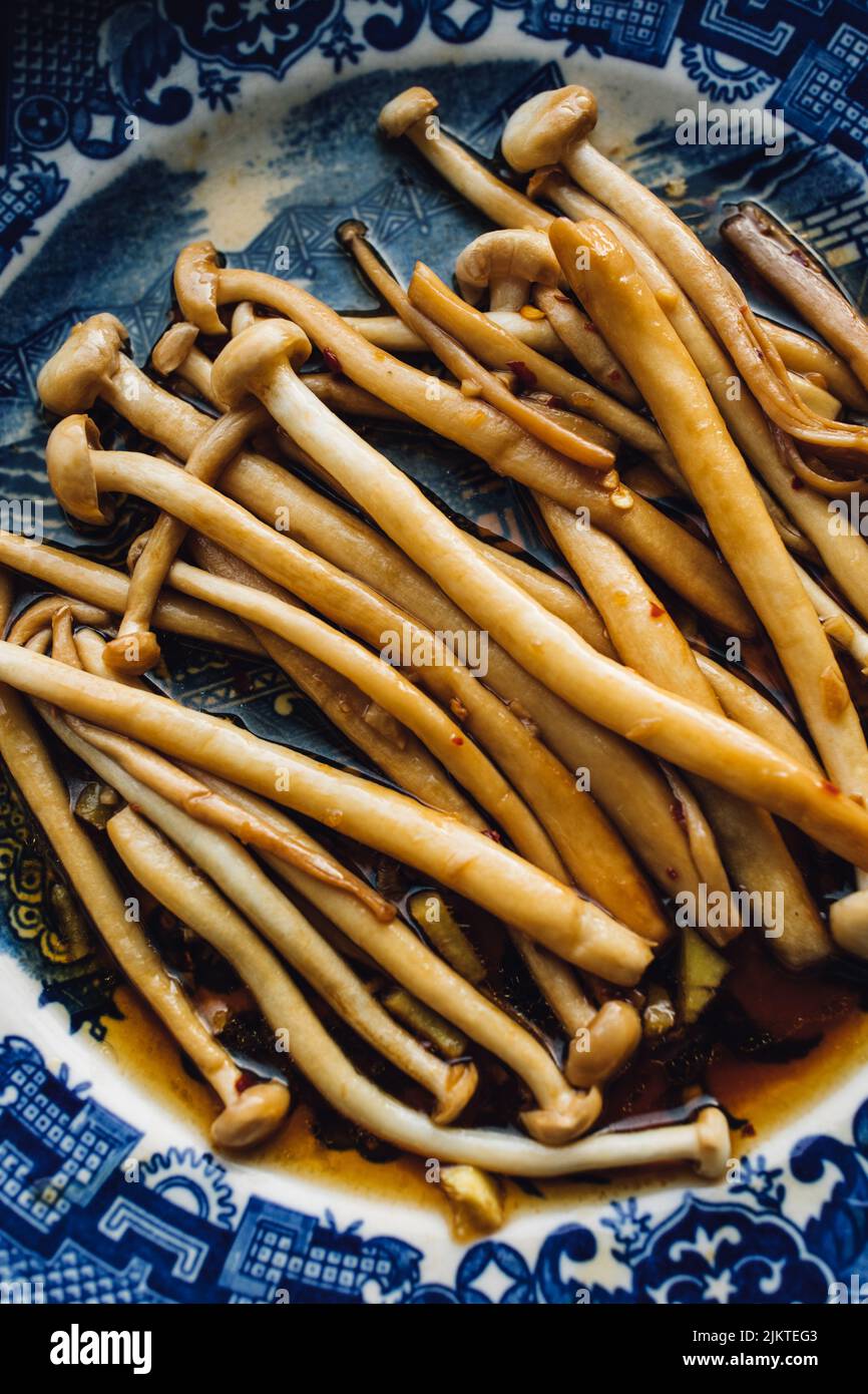 Sautierte Enoki-Pilze mit Knoblauch, Sesamöl, Sojasauce, ostasiatische Küche auf blauem und weißem japanischem Teller Stockfoto