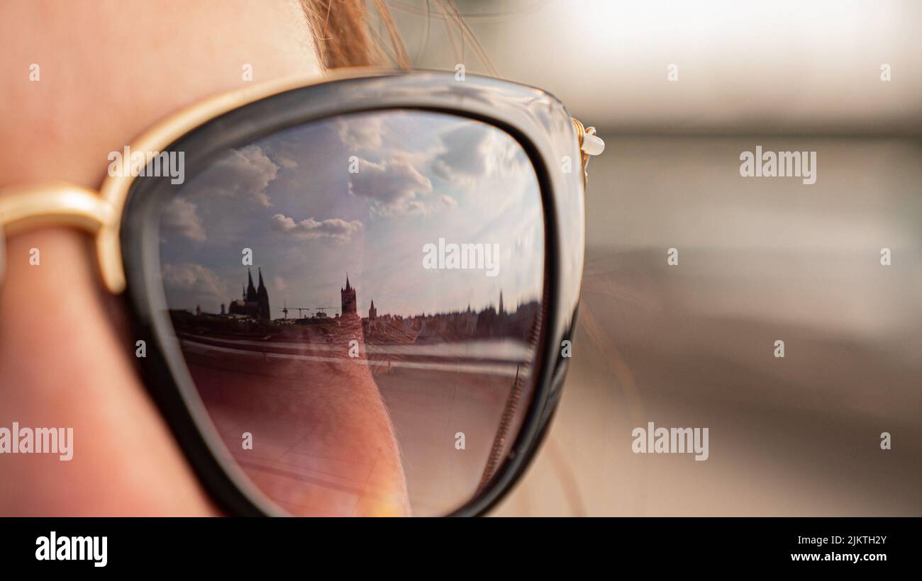 Ein Blick auf einen Teil der Sonnenbrille, der von einer Frau getragen wird, die nach vorne blickt und sich der Himmel im Glas widerspiegelt Stockfoto