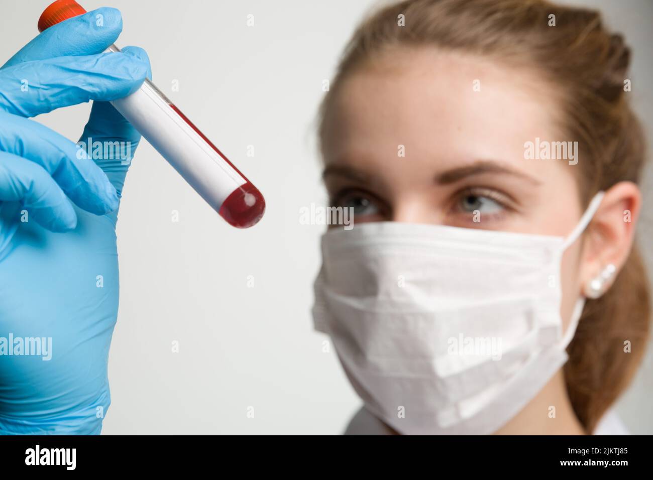 Eine junge Frau mit medizinischer Gesichtsmaske und medizinischen Handschuhen wird mit einem Bluttestrohr umgeht Stockfoto