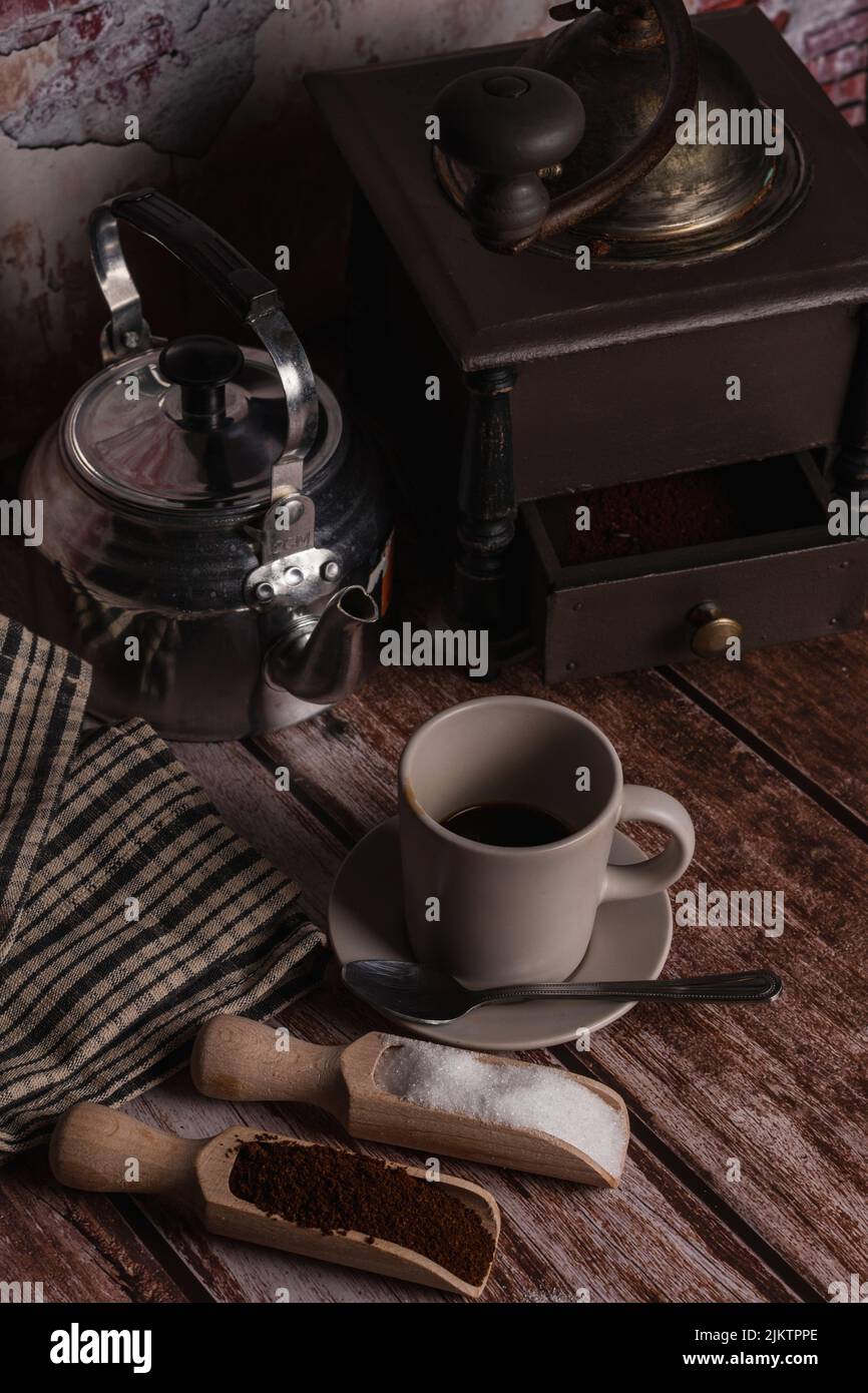 Kaffeetasse mit Milchkännchen, Mahlwerk und Holzlöffeln mit Zucker und gemahlenem Kaffee auf einem Holztisch mit Backsteinwand-Hintergrund Stockfoto