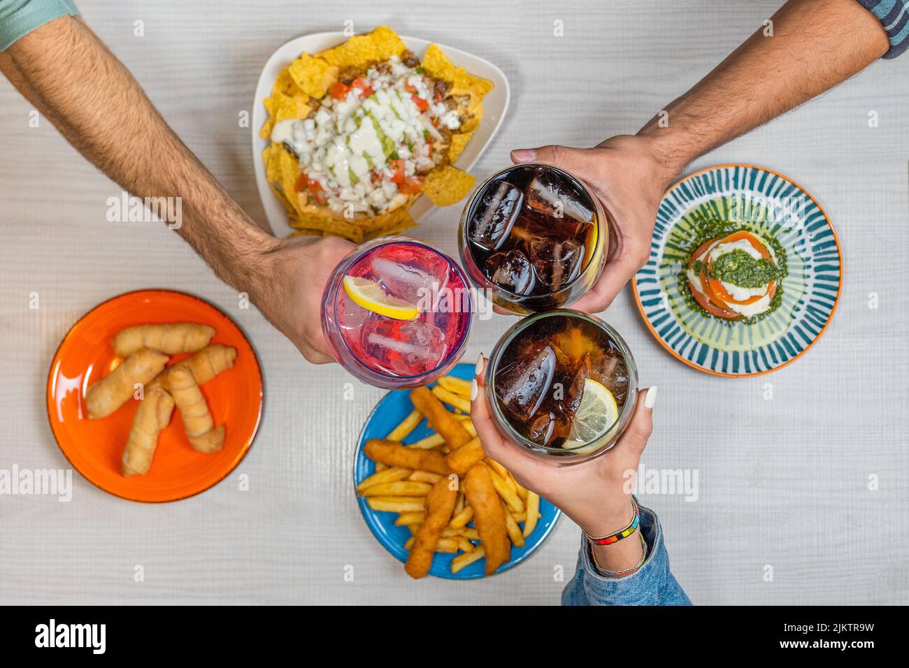 Eine Draufsicht von Händen Toasten mit verschiedenen alkoholischen Getränken auf dem Tisch mit Platten von Lebensmitteln Stockfoto