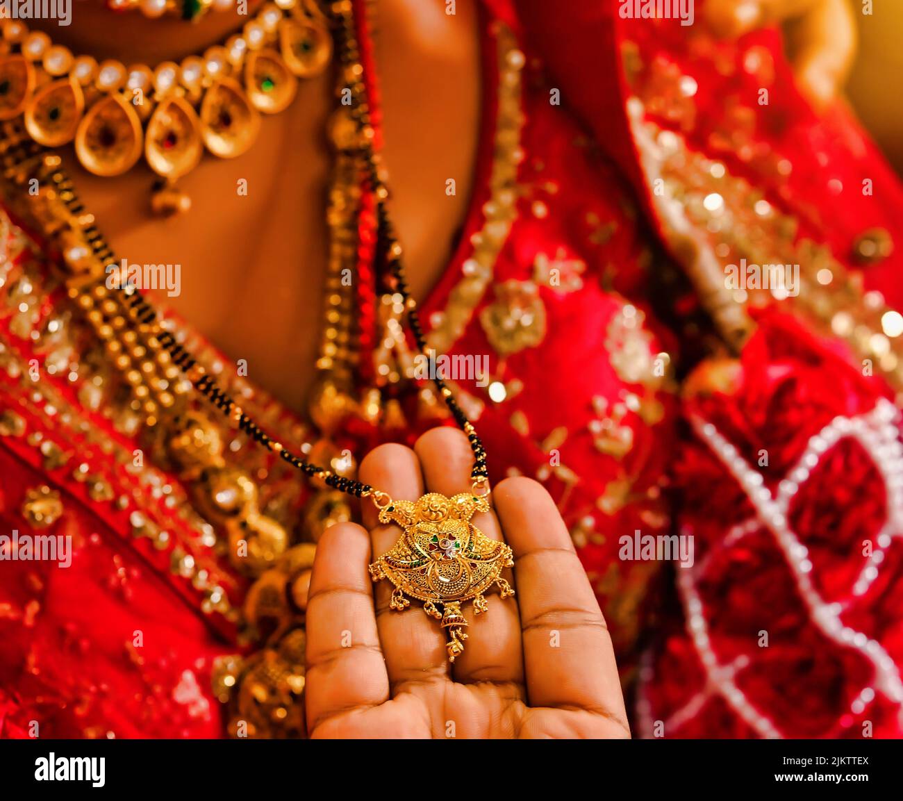 Eine Nahaufnahme der Hand des Bräutigams, der die indische Hochzeitskette (mangala Sutra) hält, nachdem er sie um den Hals der Braut gebunden hatte Stockfoto