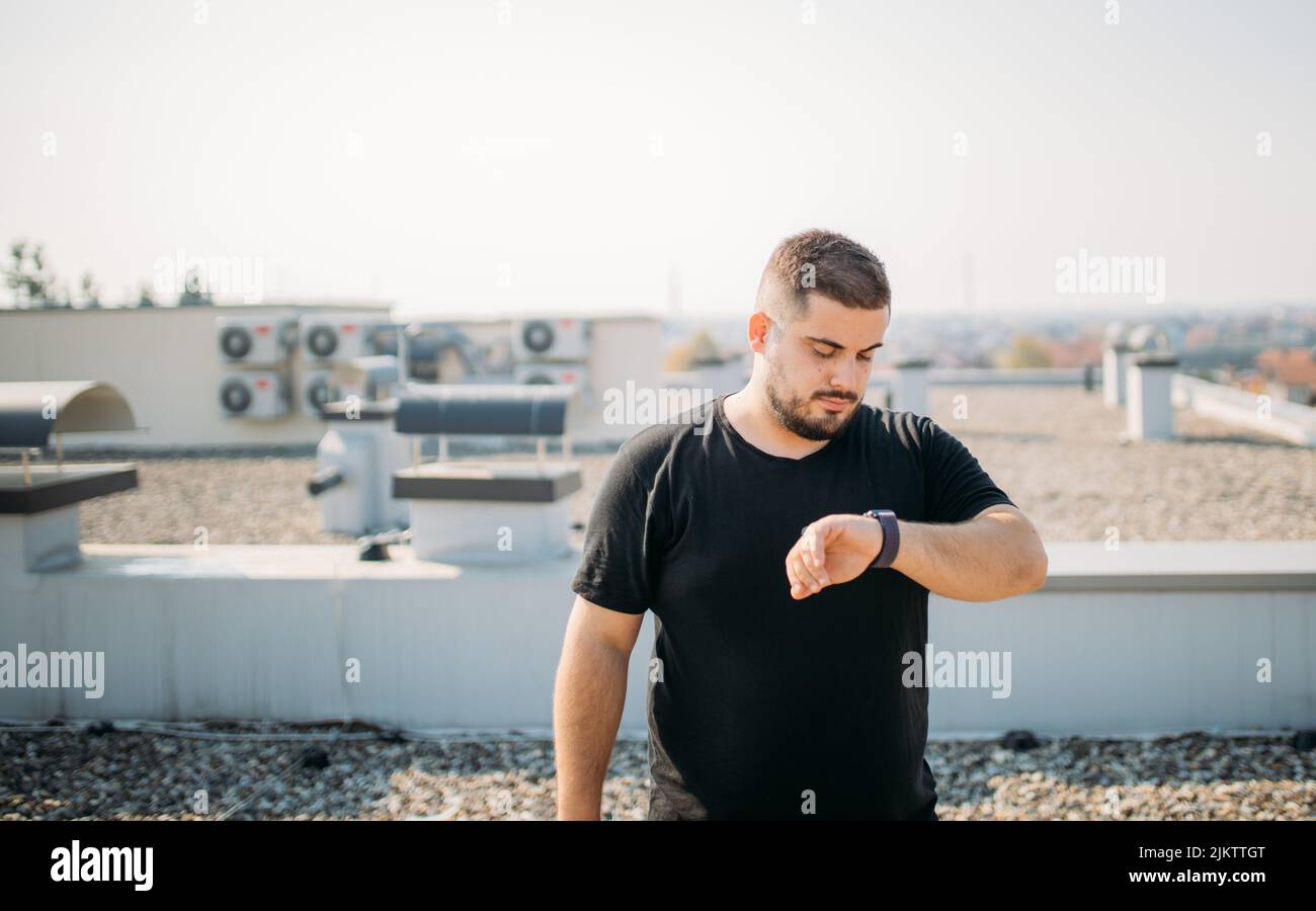 Eine schöne Aufnahme eines kühlen kaukasischen Mannes in einem schwarzen T-Shirt, das die Zeit mit einem hellen Himmel im Hintergrund überprüft Stockfoto