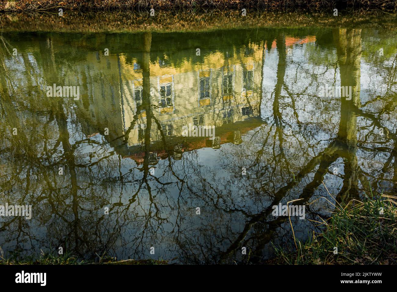 Ein Blick auf einen Teich, der ein Wohnhaus und blattlose Bäume widerspiegelt. Stockfoto