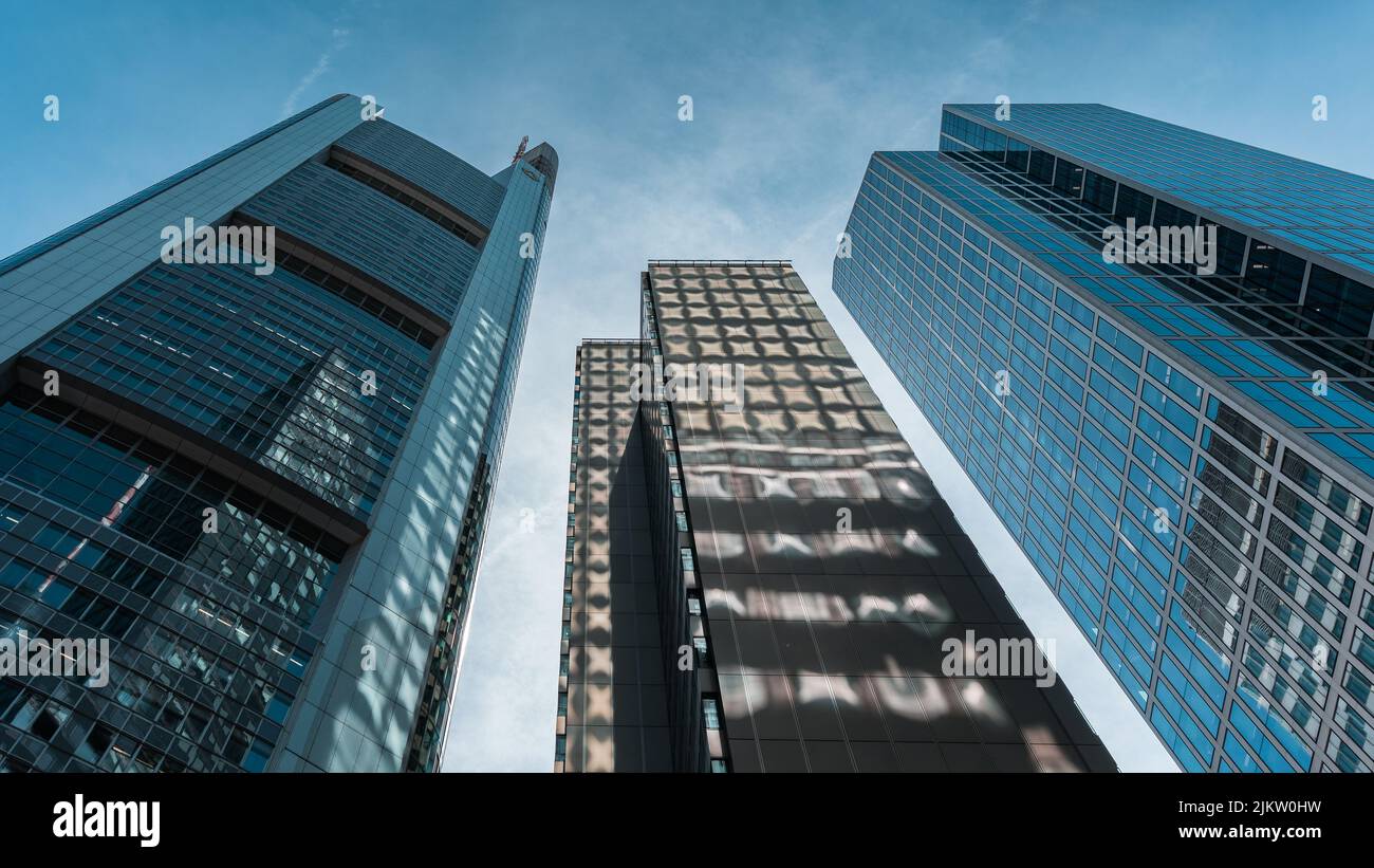 Ein niedriger Blickwinkel auf hohe Wolkenkratzer mit Glasfenstern vor dem blauen Himmel in Frankfurt, Deutschland Stockfoto