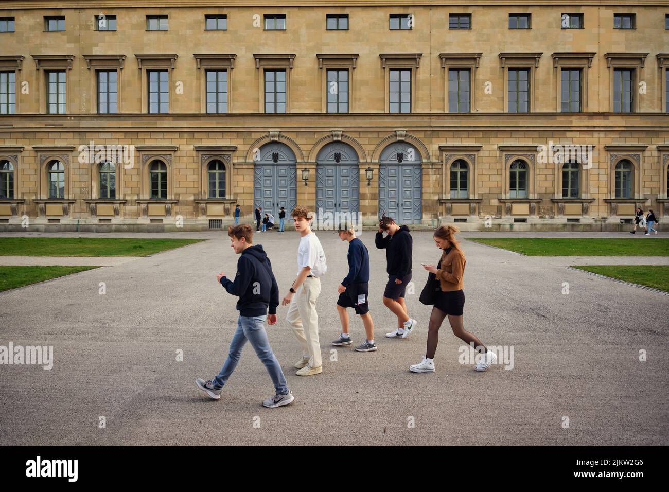 Eine Gruppe junger Freunde, die durch die Münchner Altstadt mit historischem Bauhintergrund spazieren. Freunde treffen sich im Frühling Stockfoto