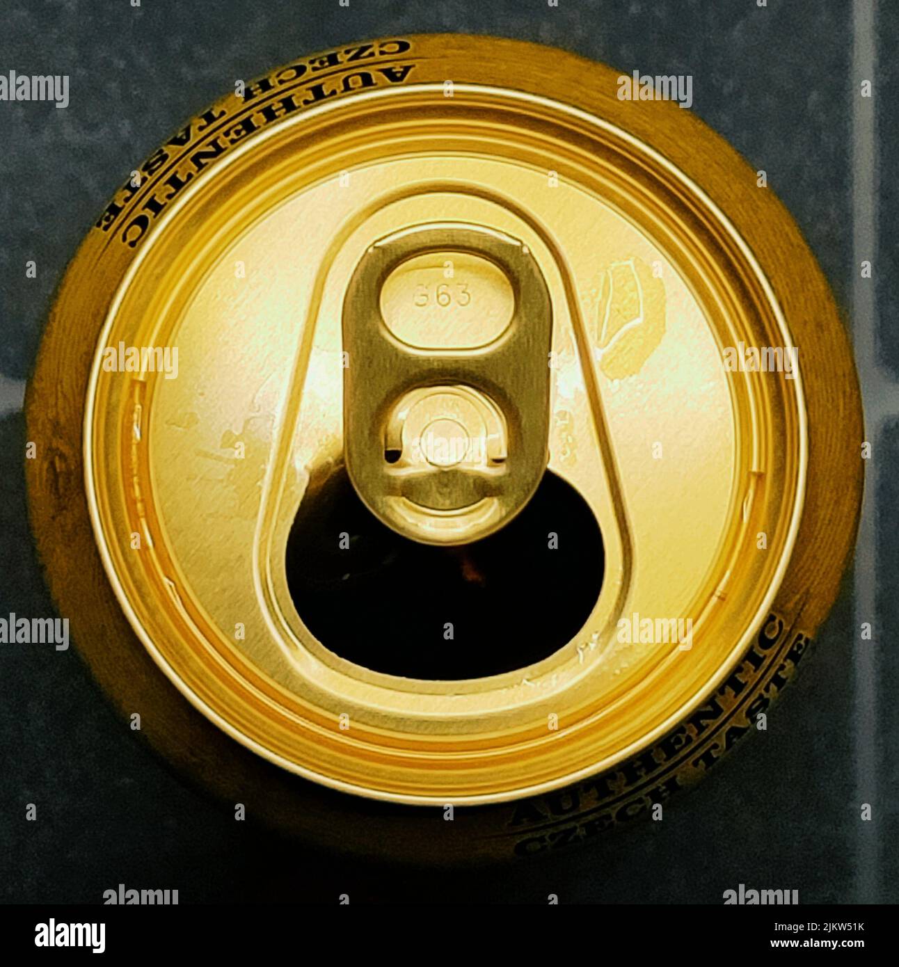 Offene Spitze eines goldenen Bieres kann in einem oberen Winkel auf grauem Hintergrund gesehen werden. Stockfoto