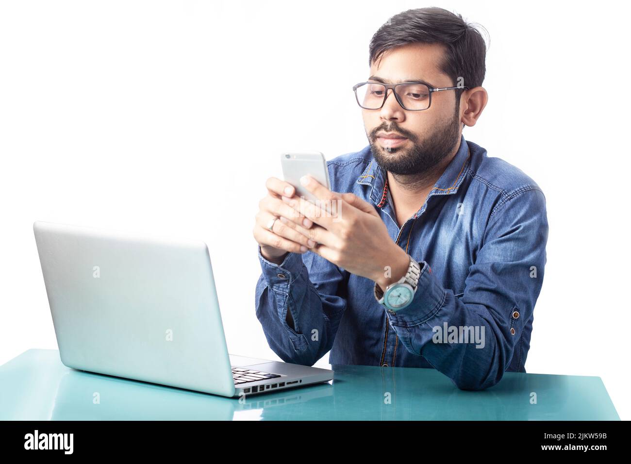 Abgelenkt arbeitende Person, die vor einem Laptop auf weißem Hintergrund auf dem Handy tippt Stockfoto