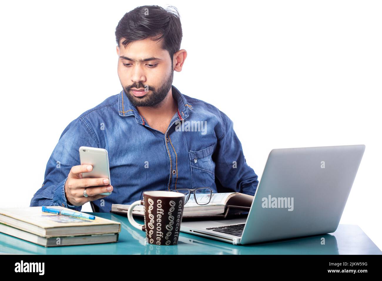 Abgelenkter Mann, der beim Arbeiten am Laptop auf den Bildschirm des Mobiltelefons schaute Stockfoto
