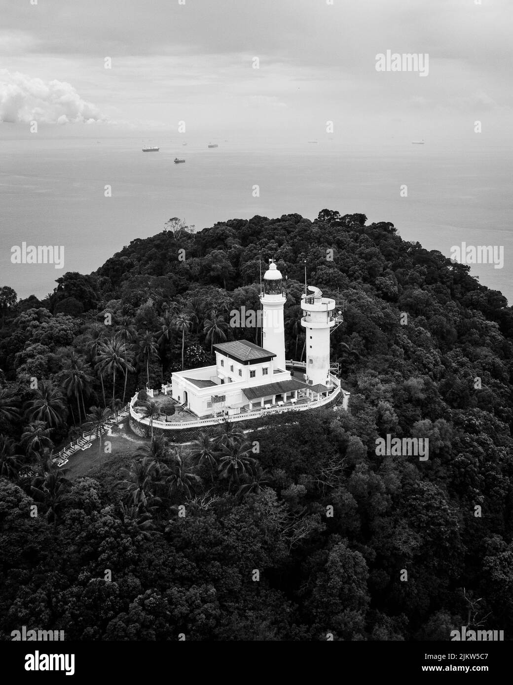 Eine Vogelperspektive auf einen Leuchtturm auf einem Berg, der mit Bäumen in Graustufen bedeckt ist Stockfoto