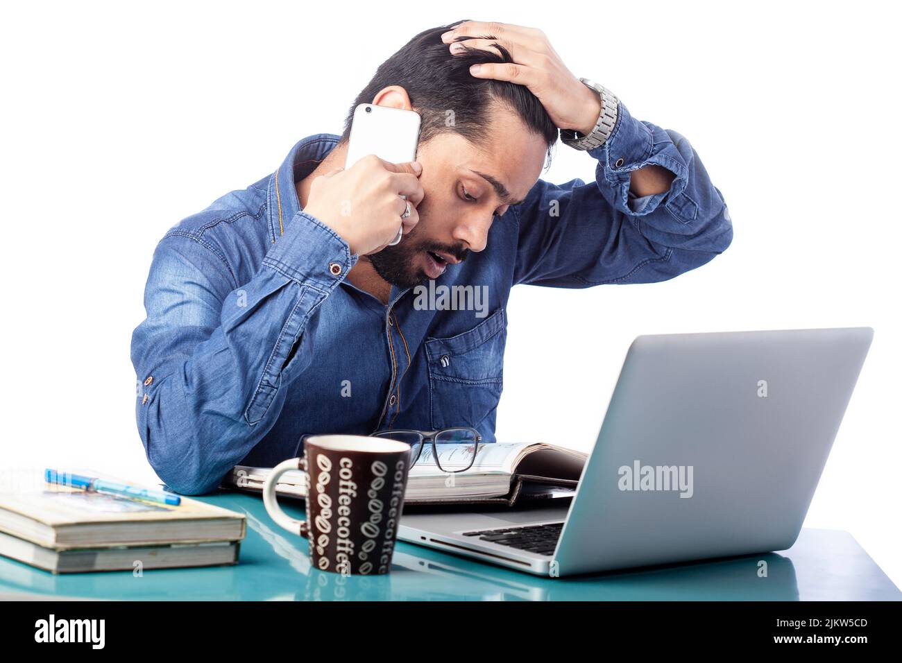 Angespannter und staunender Mann, der am Handy sprach und am Laptop arbeitete, mit Kaffeebecher auf dem Schreibtisch auf isoliertem weißem Hintergrund Stockfoto