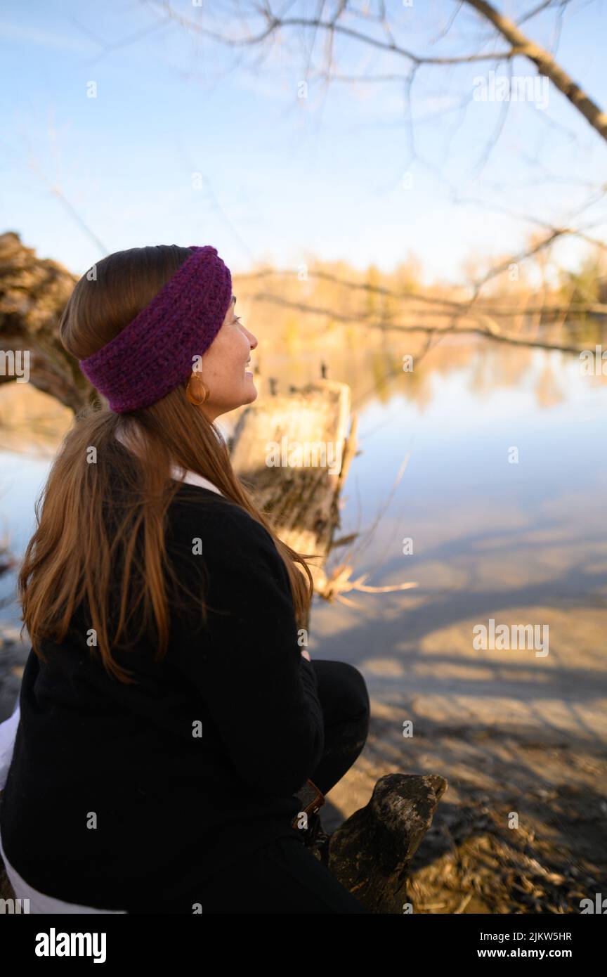 Ein Porträt einer Frau mit natürlichem blondem Haar, die an einem Frühlingstag mit einem violetten Haarreif in die Ferne auf einen Fluss blickt Stockfoto