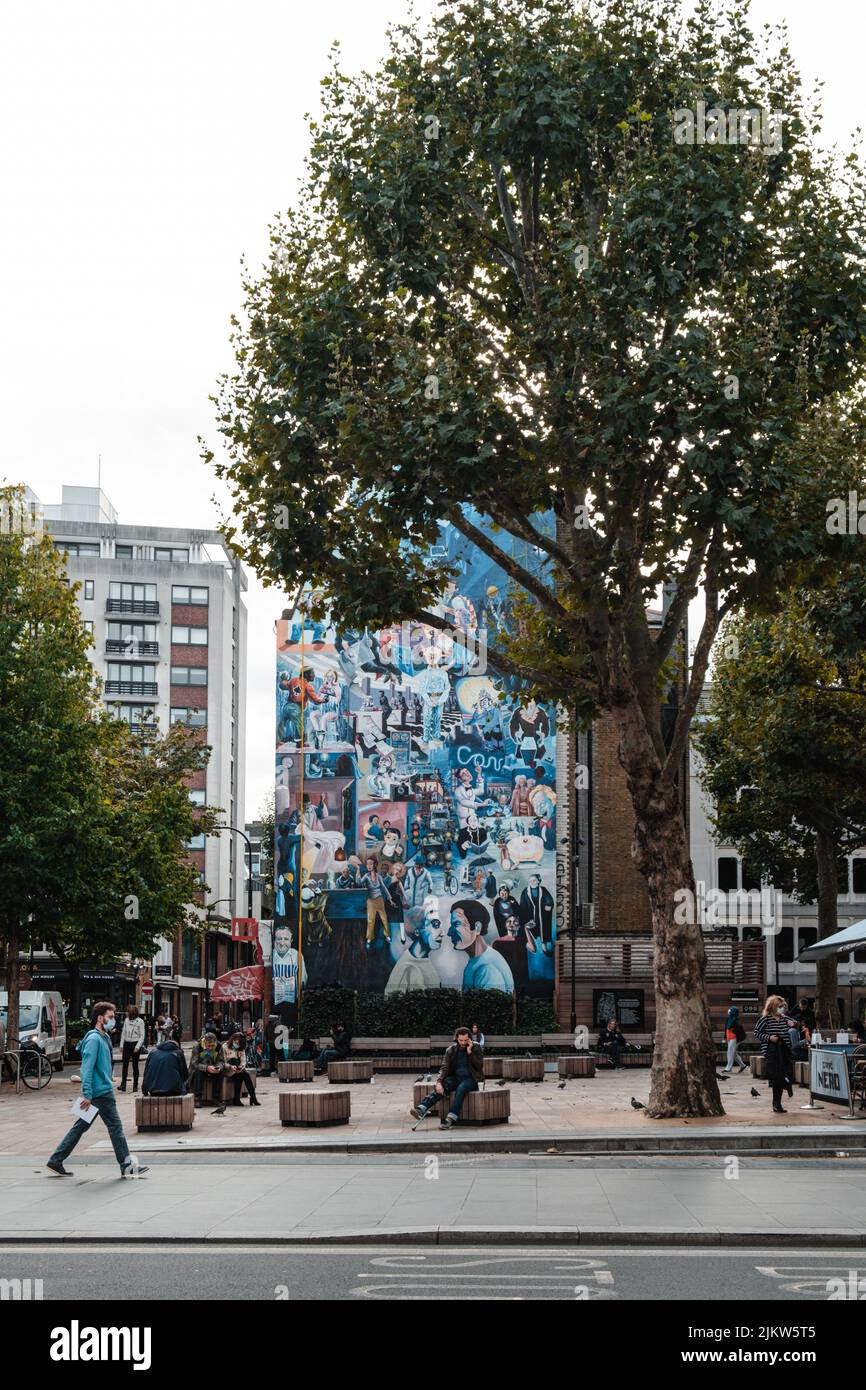 Eine vertikale Aufnahme eines Gebäudes mit einem gemalten Wandgemälde in der Nähe eines hohen Baumes in London, Großbritannien Stockfoto