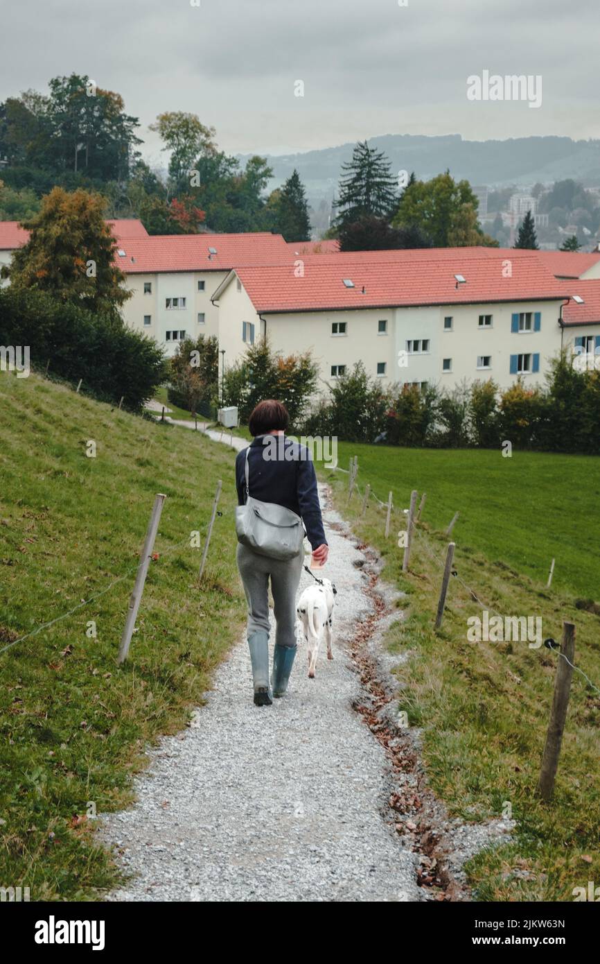 Eine vertikale Aufnahme einer Frau, die mit ihrem Hund in St. Gallen läuft Stockfoto