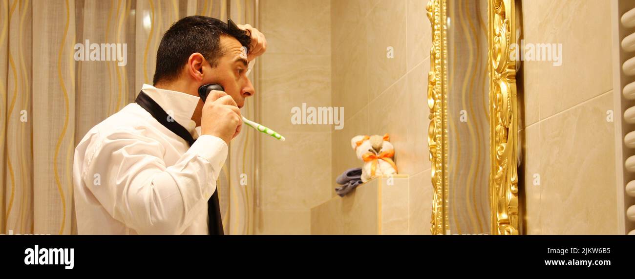 Eine Seitenansicht eines kaukasischen Mannes, der mehrere Aktionen gleichzeitig im Badezimmer macht Stockfoto