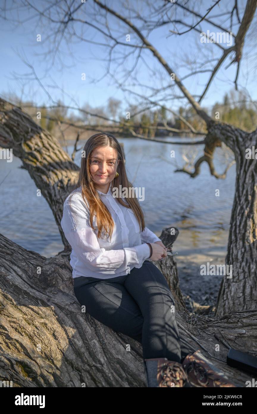 Eine selbstbewusste Frau im Freien vor einem Fluss sitzt auf einem Ast Stockfoto