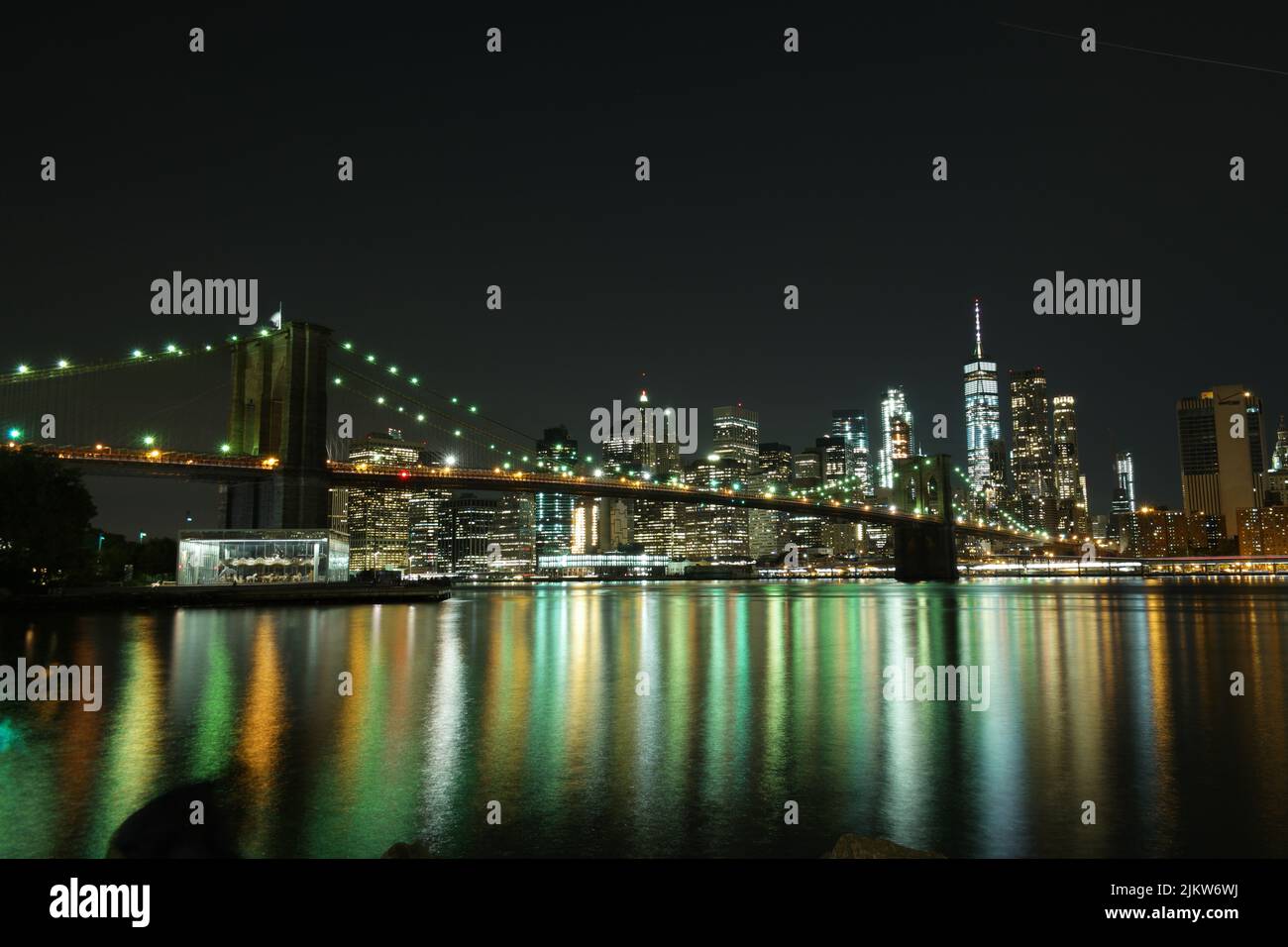 Die Brooklyn Bridge und die Skyline von New York City mit den Lichtreflexen in der Bucht bei Nacht Stockfoto