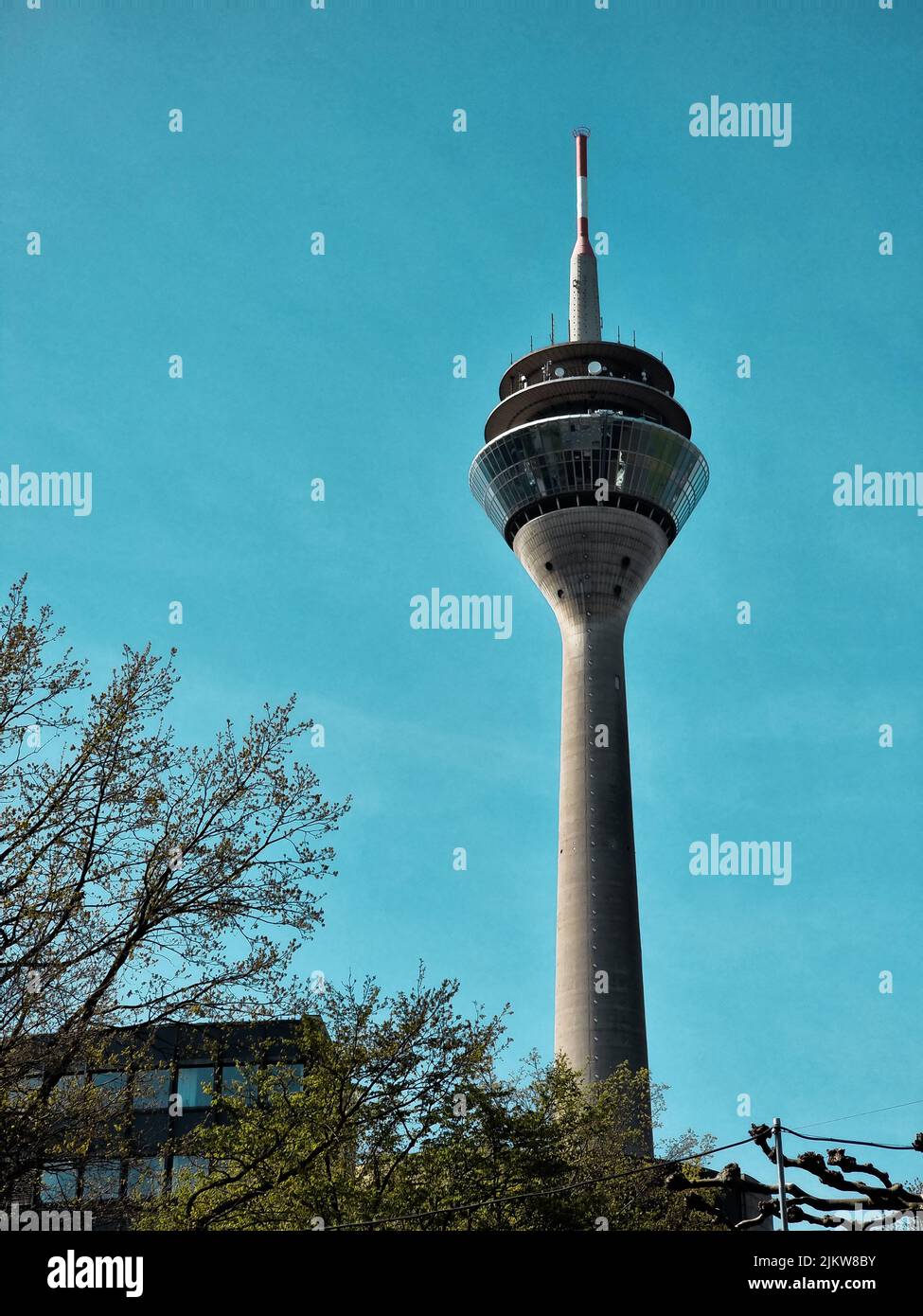 Eine vertikale Aufnahme des Rheinturms an einem blauen Himmelstag mit Bäumen in der Umgebung Stockfoto