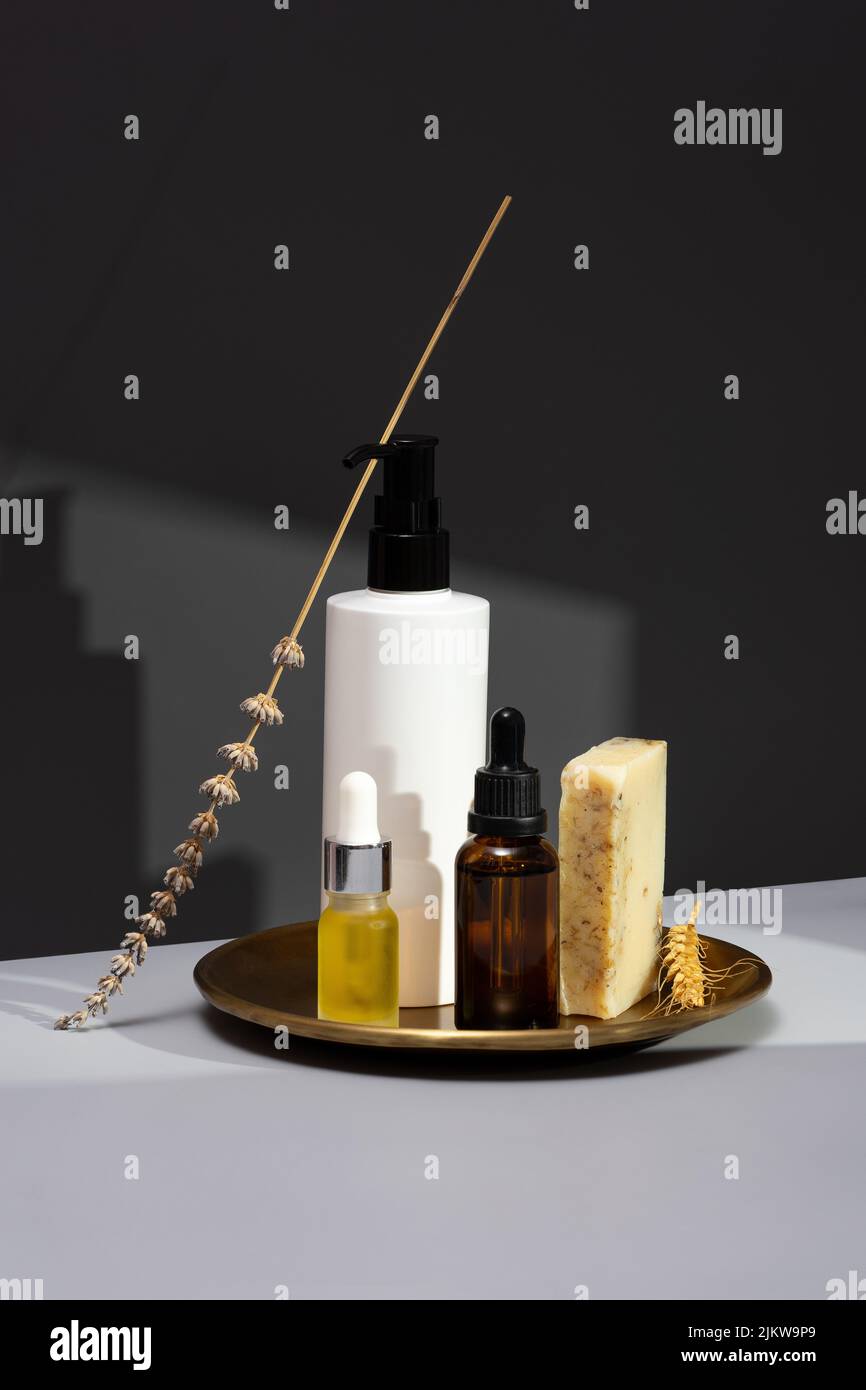 Kreatives Stillleben mit Naturkosmetik. Set aus ätherischen Ölen, handgefertigter Seife und getrocknetem Lavendel auf dunkelgrauem Hintergrund. Das Konzept der Selbstversorgung Stockfoto