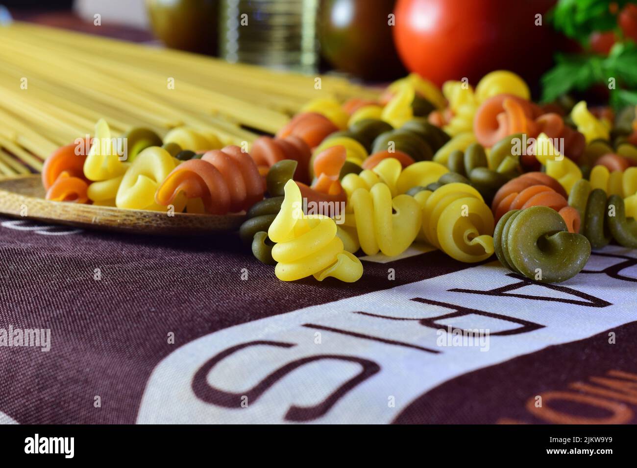 Eine Nahaufnahme von farbigen Nudeln, die auf einem Tisch mit Tomaten im Hintergrund verstreut sind Stockfoto