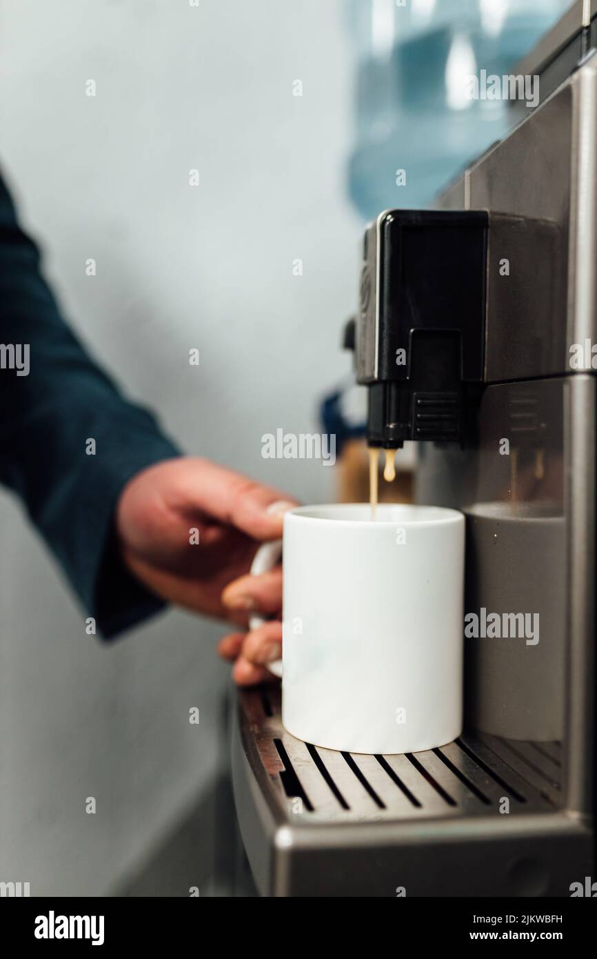 Vertikale Nahaufnahme des Geschäftsmannes, der Kaffee aus der Kaffeemaschine im Büro zubereitet Stockfoto