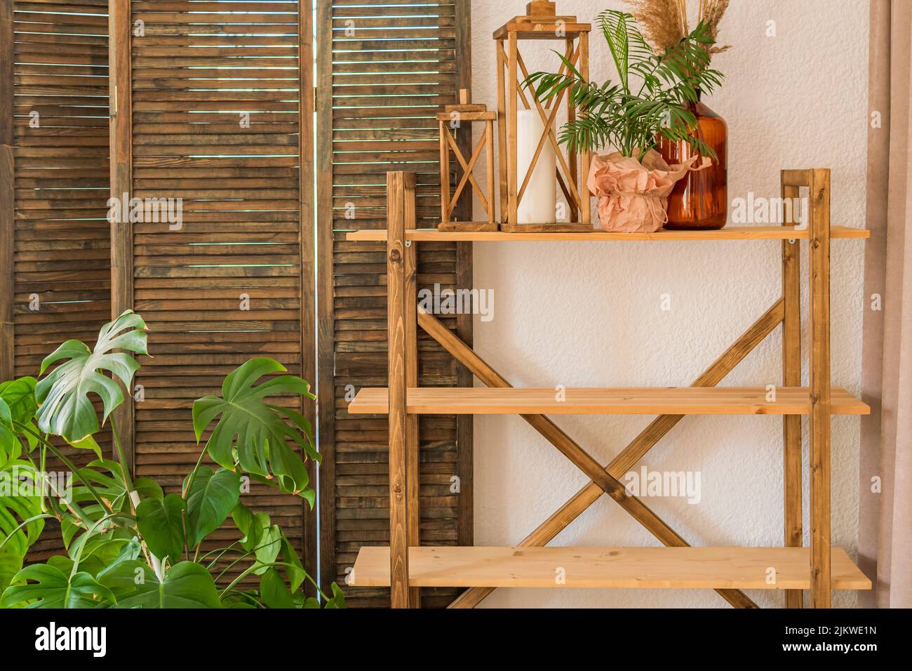Dekoriertes Zimmer: Holzregal mit Laternen mit Kerzen, Vase mit Blume vor dem Hintergrund der Wand und einem Bildschirm. Gemütlich eingerichtetes Wohnzimmer. Stockfoto