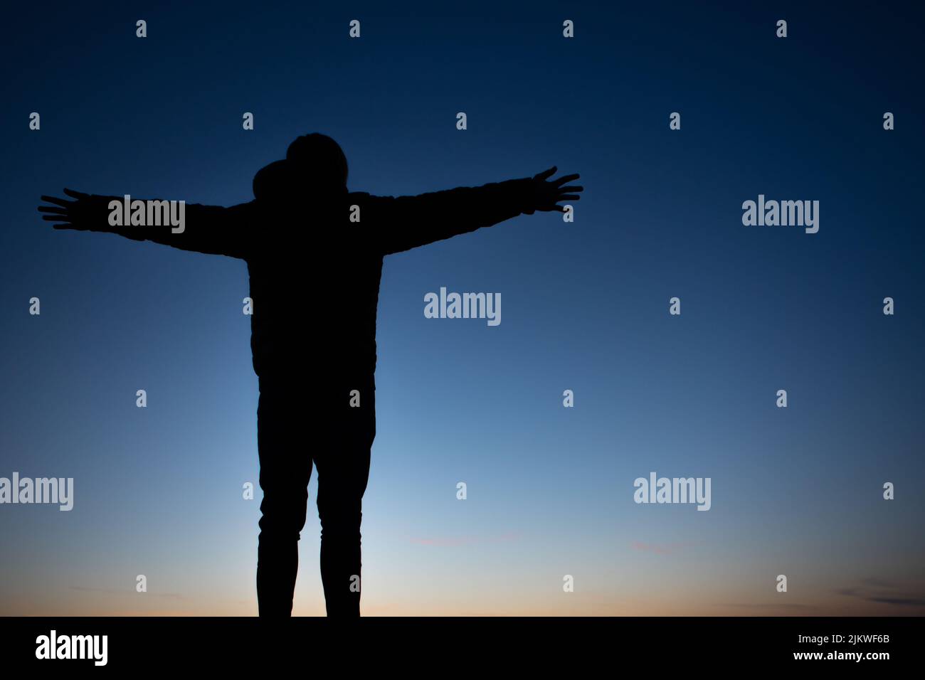 Rückansicht einer Silhouette einer Person mit offenen Händen, die den Sonnenuntergang und die Freiheit genießt Stockfoto