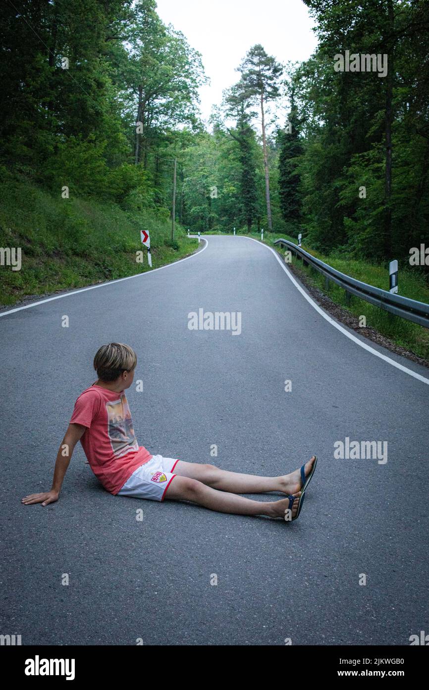 Eine vertikale Aufnahme eines Mannes, der auf einer von Bäumen umgebenen Autobahn sitzt. Stockfoto