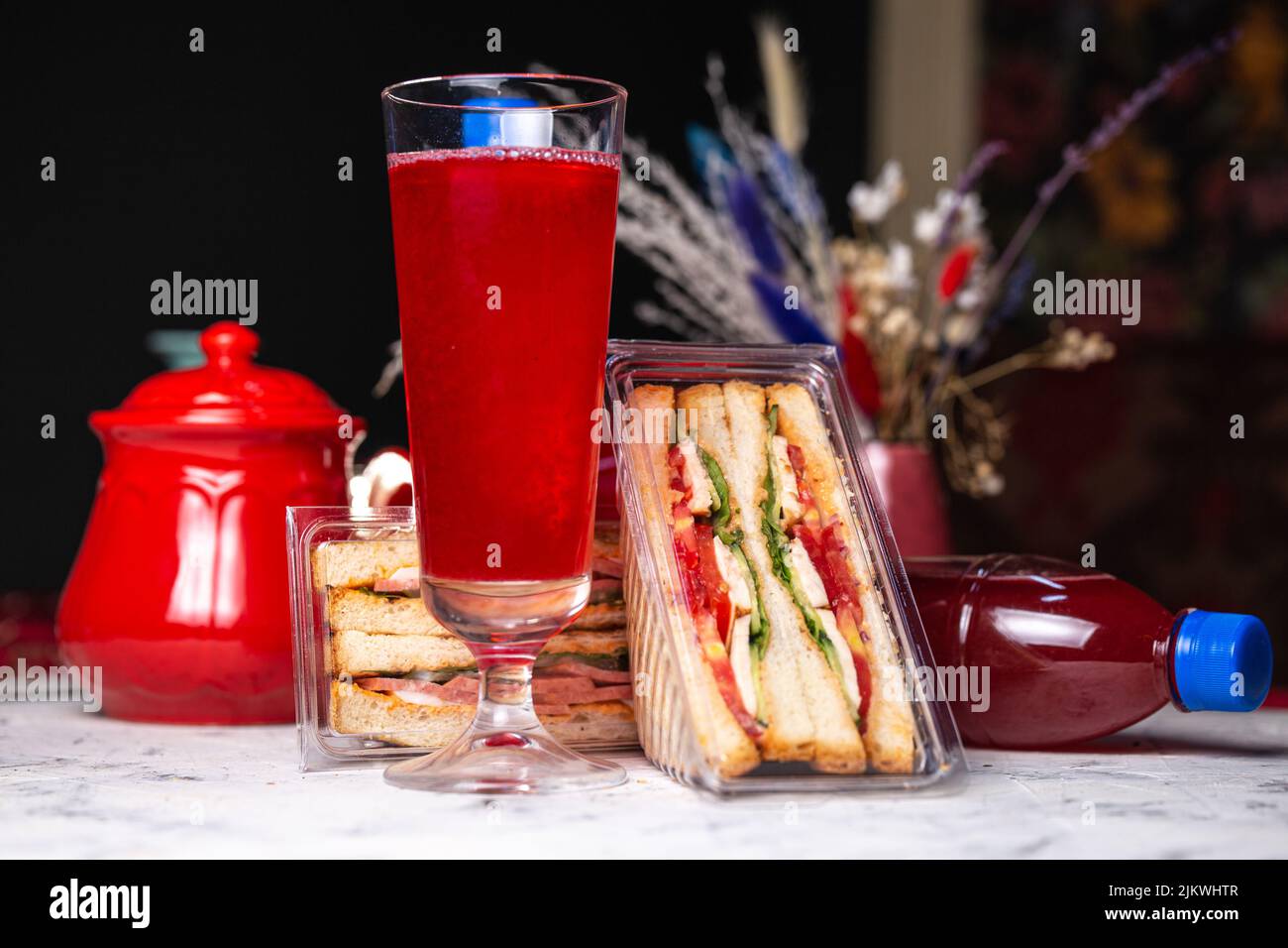 Sandwich mit Füllung in einer Plastikverpackung und einem Getränk auf dem Tisch. Stockfoto