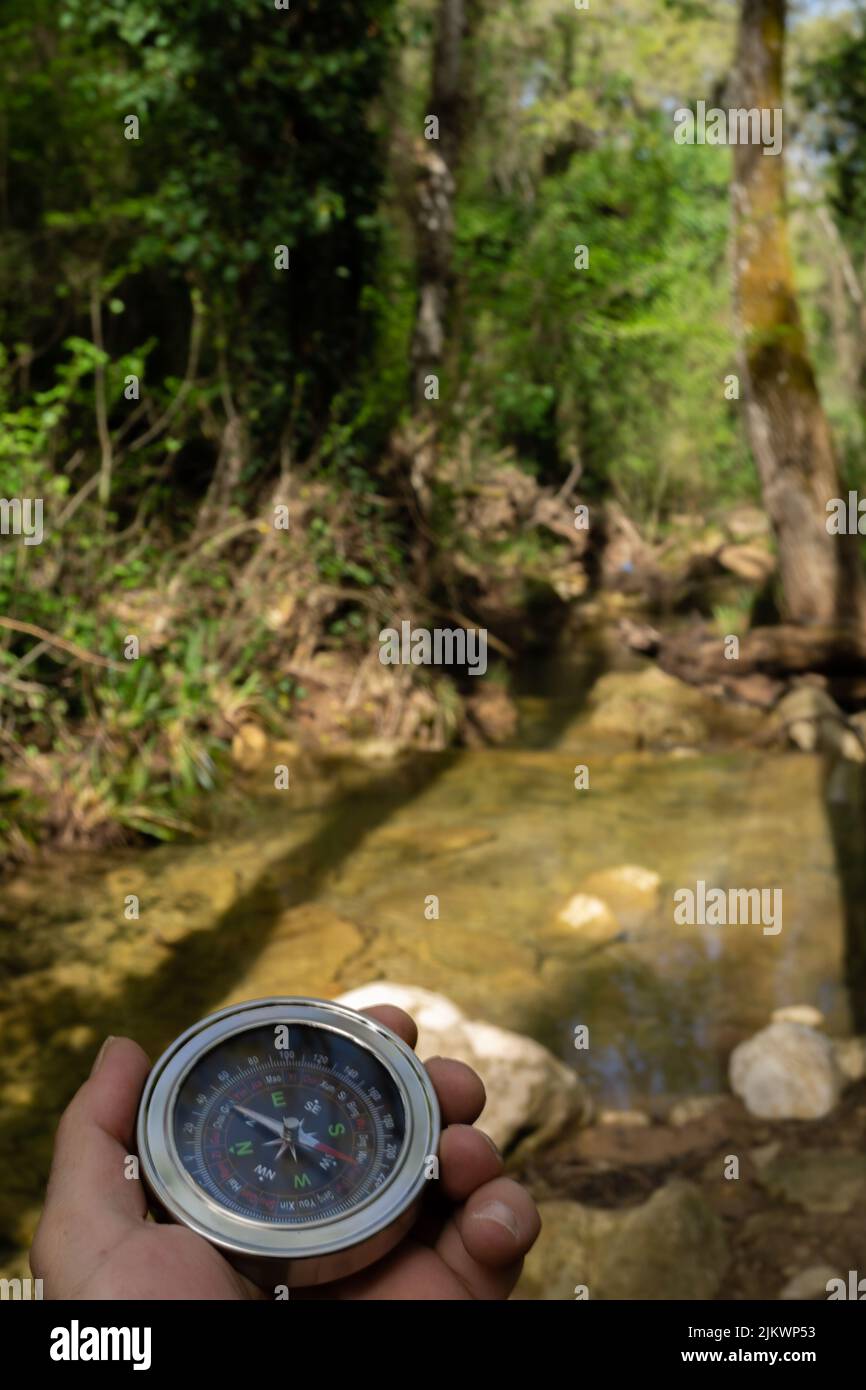 Die Hand des Mannes hält einen Kompass im Wald mit einem Gebirgsfluss im Hintergrund Stockfoto