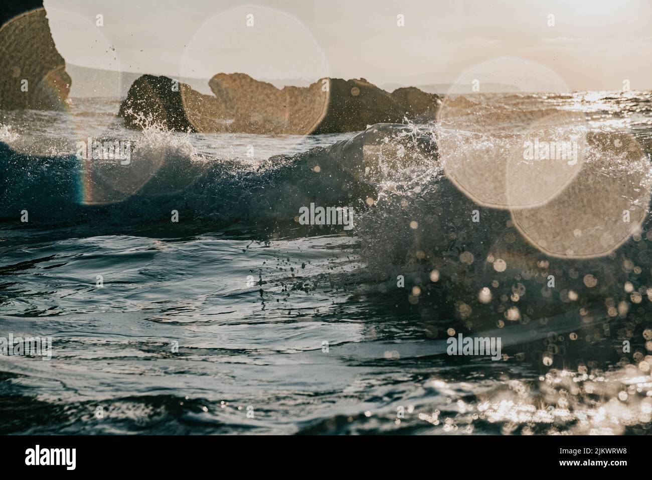 Eine Nahaufnahme von plätschernden Wellen auf dem Meer gegen eine helle Sonne mit Bokeh-Effekt Stockfoto